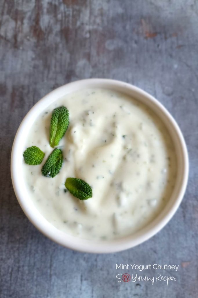 A bowl of mint yogurt chutney with mint leaves garnish.