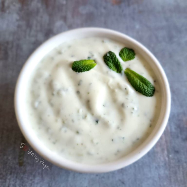 Mint yogurt chutney in a white round bowl and garnished with some mint leaves.