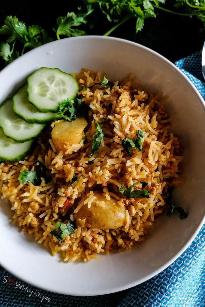 A deep plate of chicken biryani garnished with sliced cucumber and chopped cilantro.