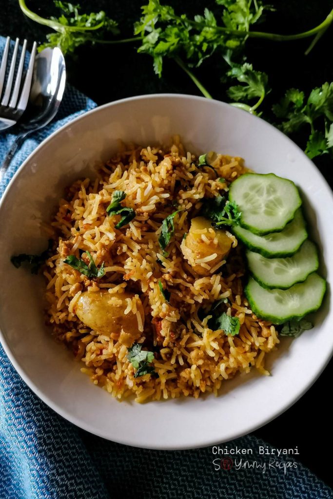 A round plate of chicken biryani rice in with sliced cucumber.