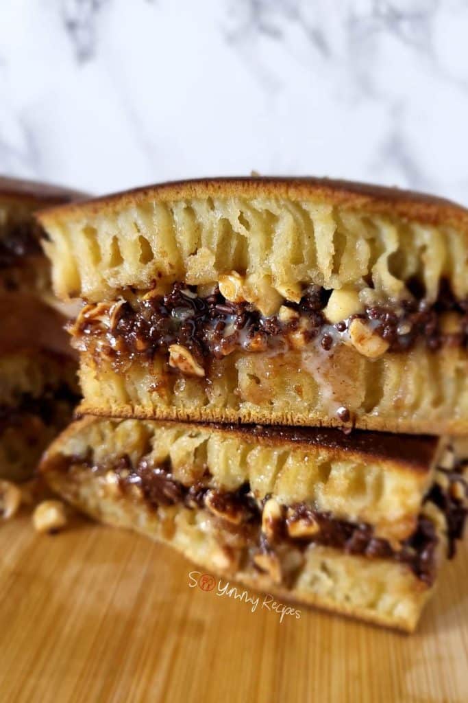 Two pieces of Martabak Manis stacked together on a wooden chopping board.