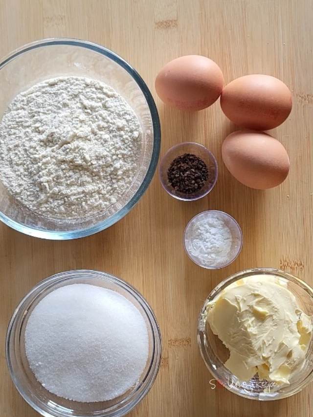 A bowl of flour, a bowl of sugar, a bowl of margarine, a bowl of baking powder, a small container of instant coffee granules, and eggs.