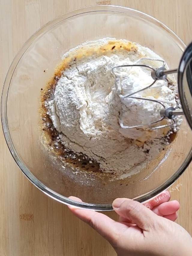 Handheld mixer in a mixing bowl of cupcake ingredients.