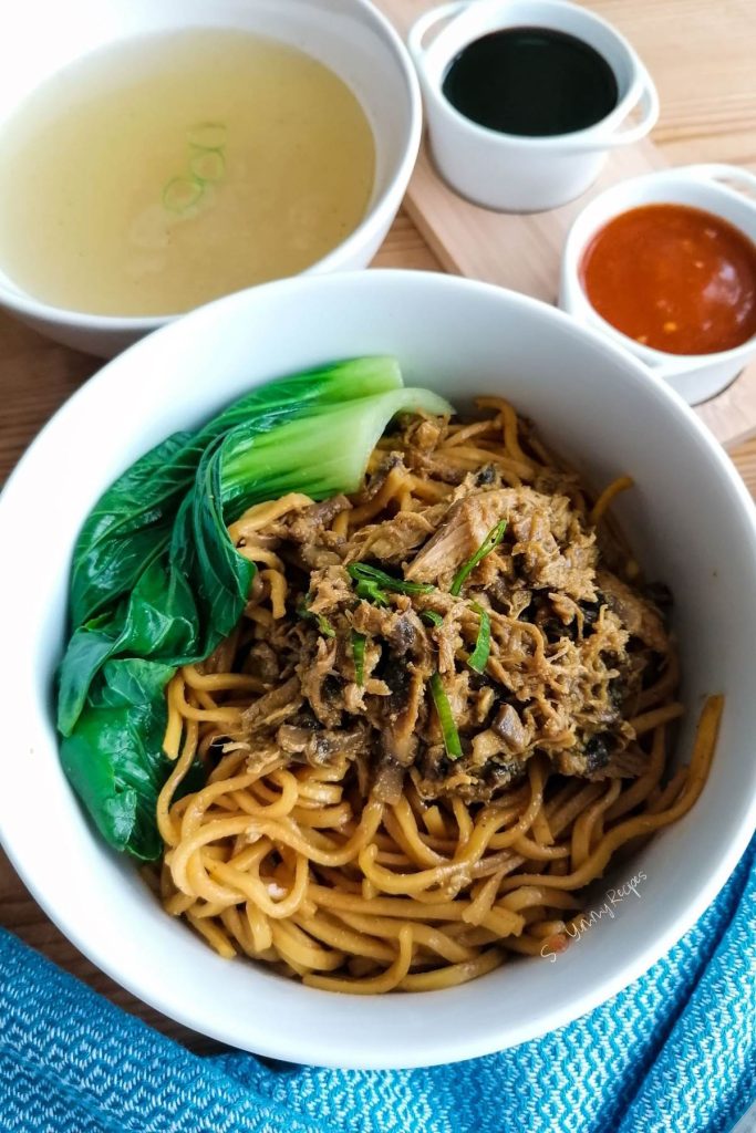 Noodles with chicken topping, pak choi, chicken broth, and a few condiment in small bowls.