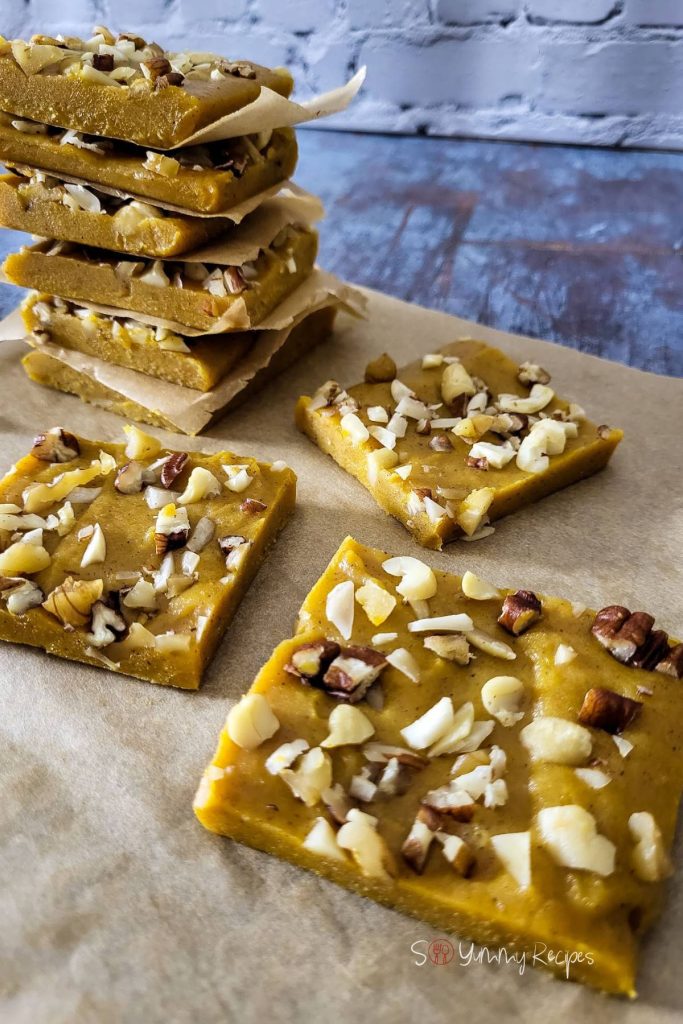 Squares of pumpkin fudge are stacked and scattered on parchment paper.