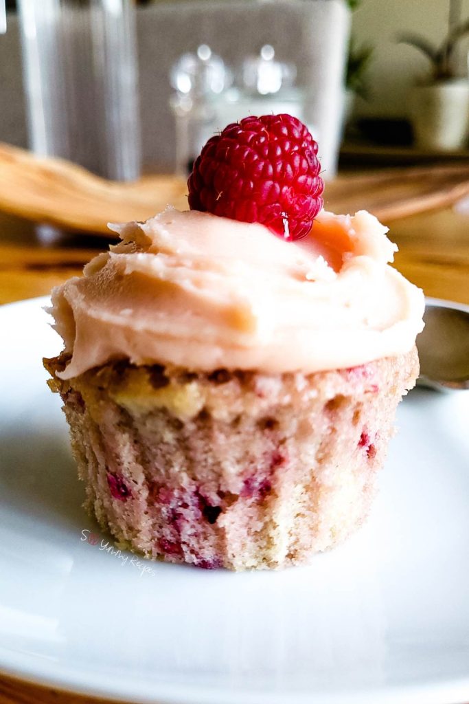 A raspberry cupcake with raspberry buttercream and a raspberry on the top.