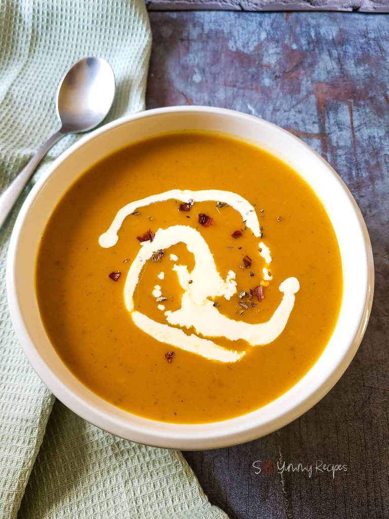 A bowl of pumpkin and sweet potato soup with a green napkin and a spoon next to it.