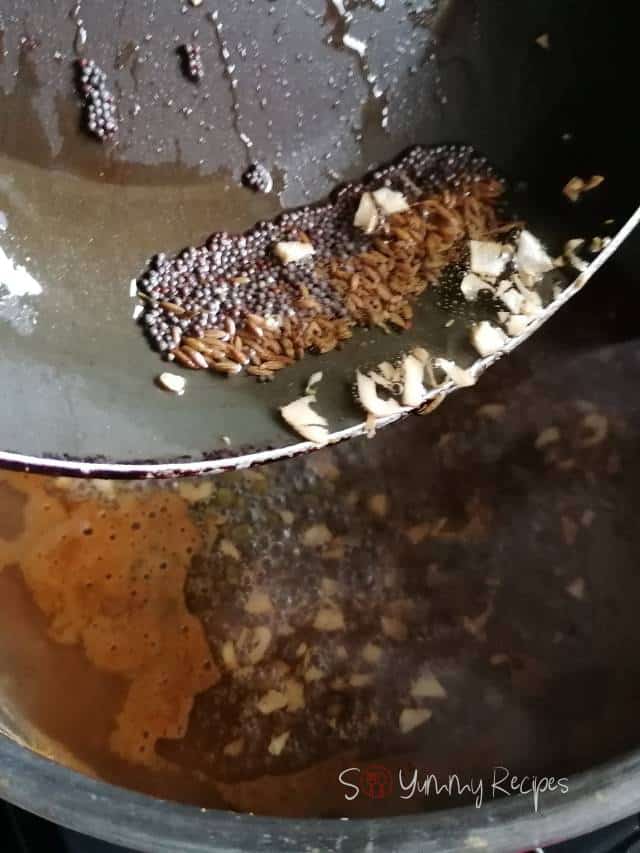 A pan of whole spices over a pan of mung bean curry.