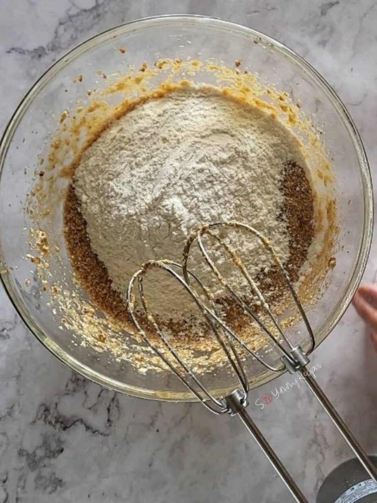 flour over wet ingredients of cake mixture in a bowl.
