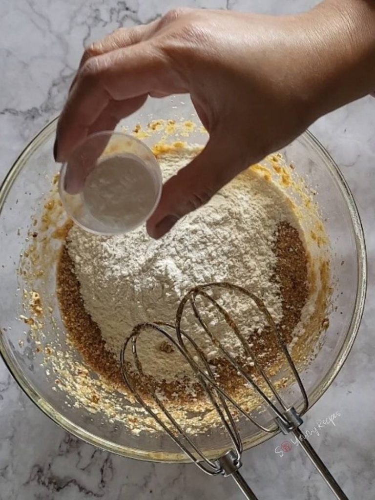 a hand holding a small container of baking powder over a bowl of cake mixture.