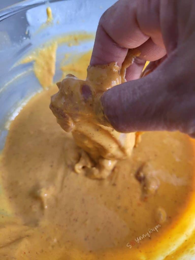 A hand dipping a chicken piece in gram flour batter.