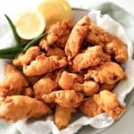 Chicken pakora pieces on a plate with lemon slices and green chilies.