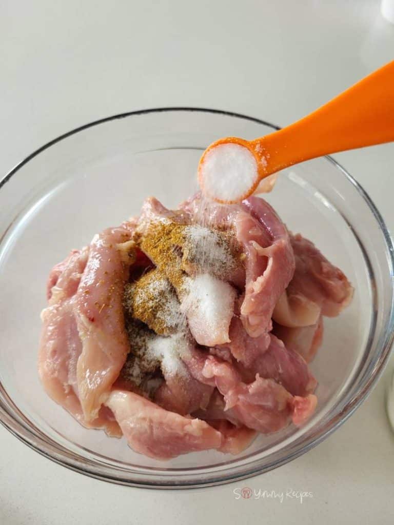 A bowl of chicken pieces and a spoon of salt over it.