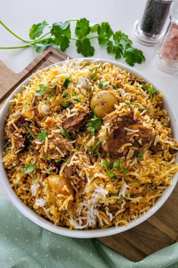 Biryani rice in a white deep plate with cilantro leaves next to it.