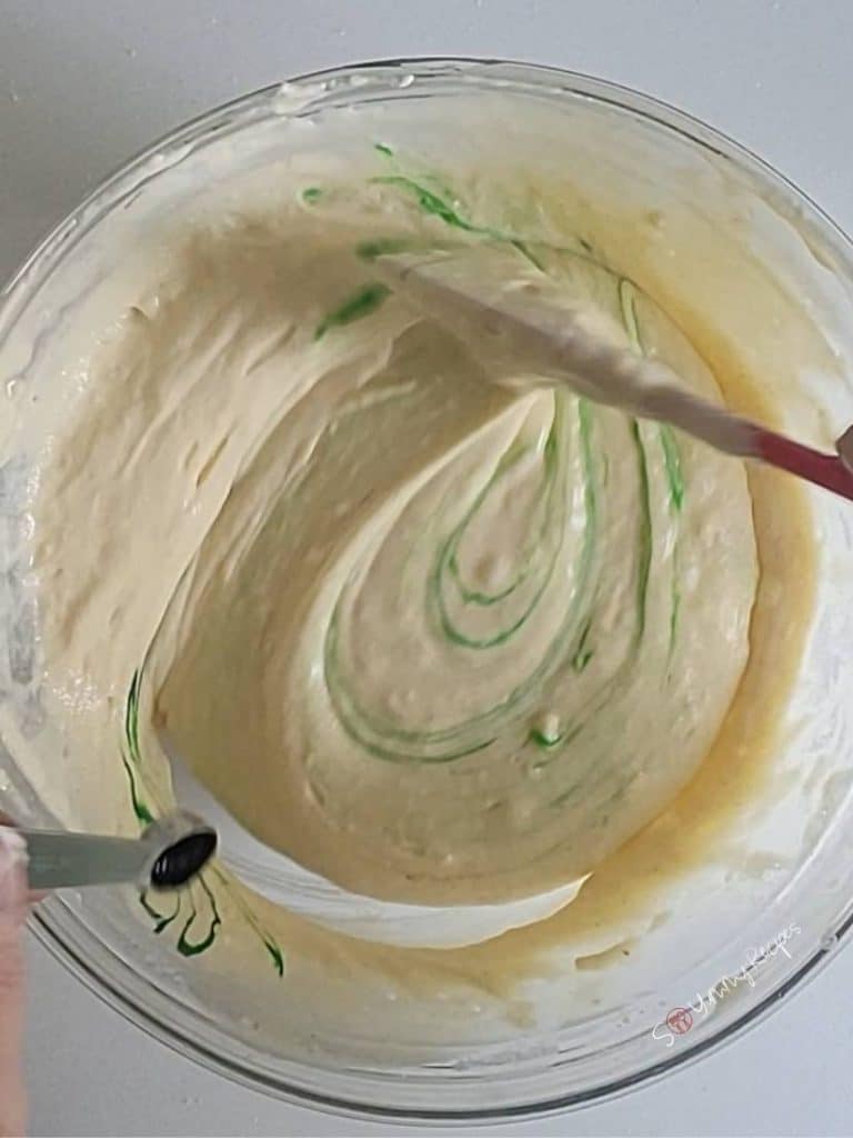 yellow cake batter tinted with green coloring and a spatula.