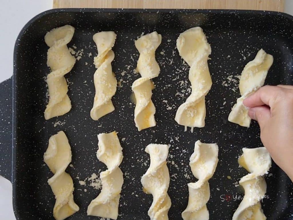 A hand sprinkle the grated cheese over pastry straws.