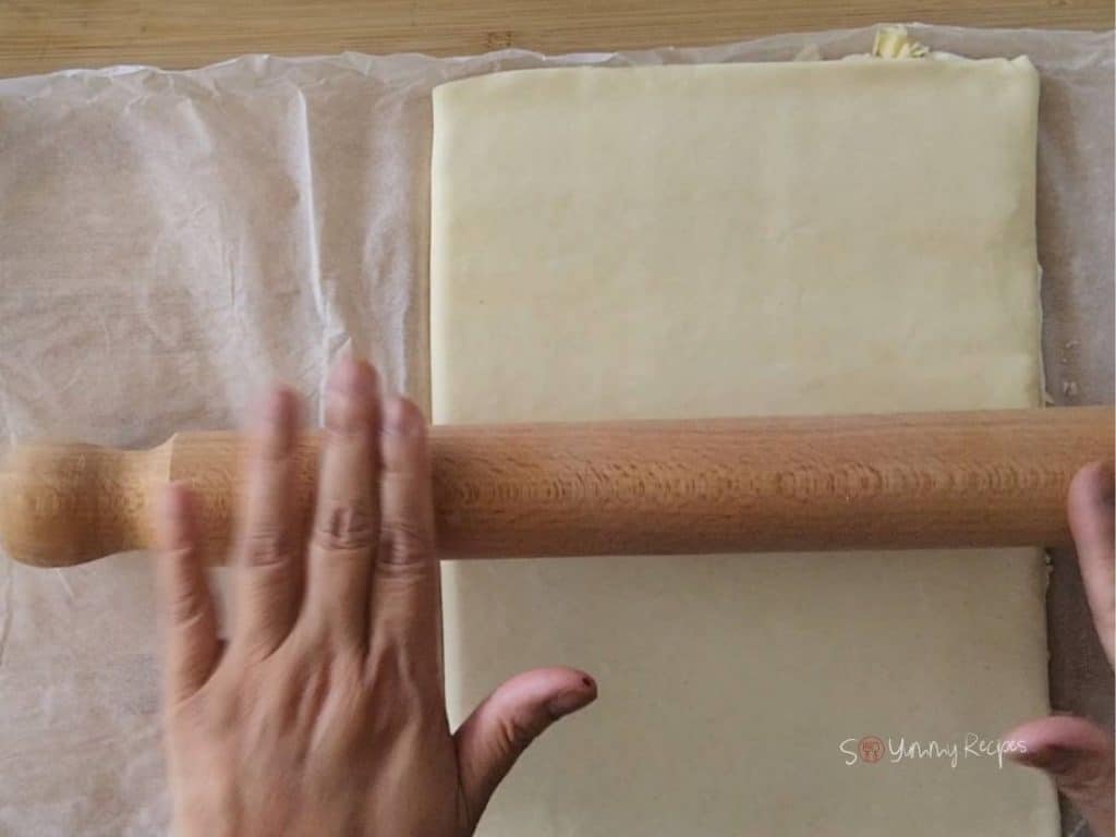 Hands roll a rolling pin over a puff pastry,