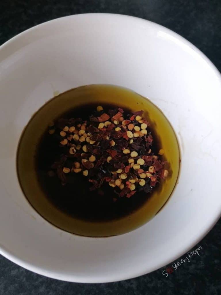 A mix of balsamic vinegar, olive oil, and chili flakes in a white bowl.