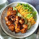 Air fryer salmon bites with teriyaki sauce and some salad on a round plate.