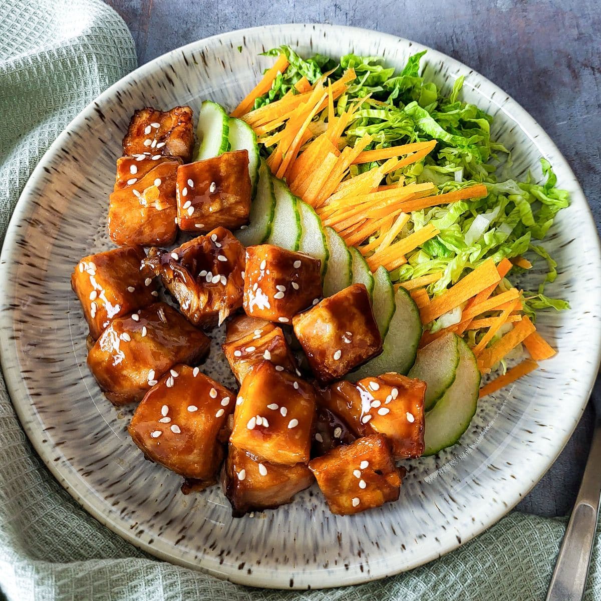 Air fryer salmon bites with teriyaki sauce and some salad on a round plate.