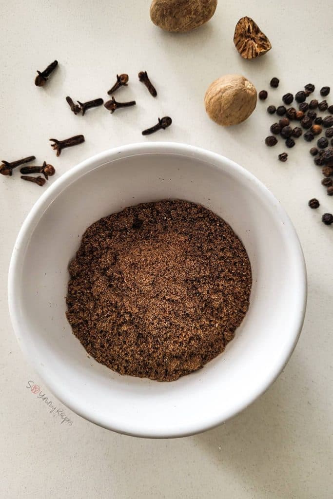 Ground spice mix in a small white bowl with some whole spices in the background.