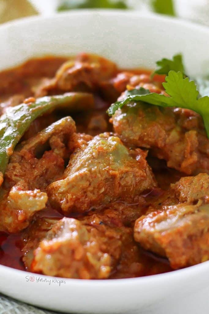 Lamb curry with tomato based gravy, garnished with green chili and coriander leaves.