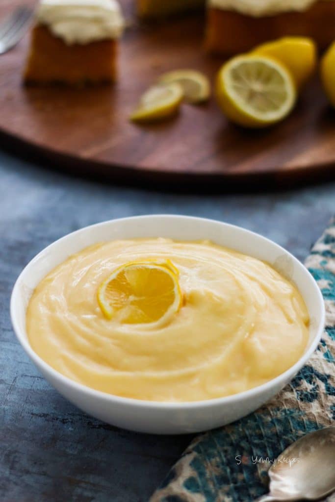 Lemon custard in a white bowl with wooden chopping board and lemon in the background.