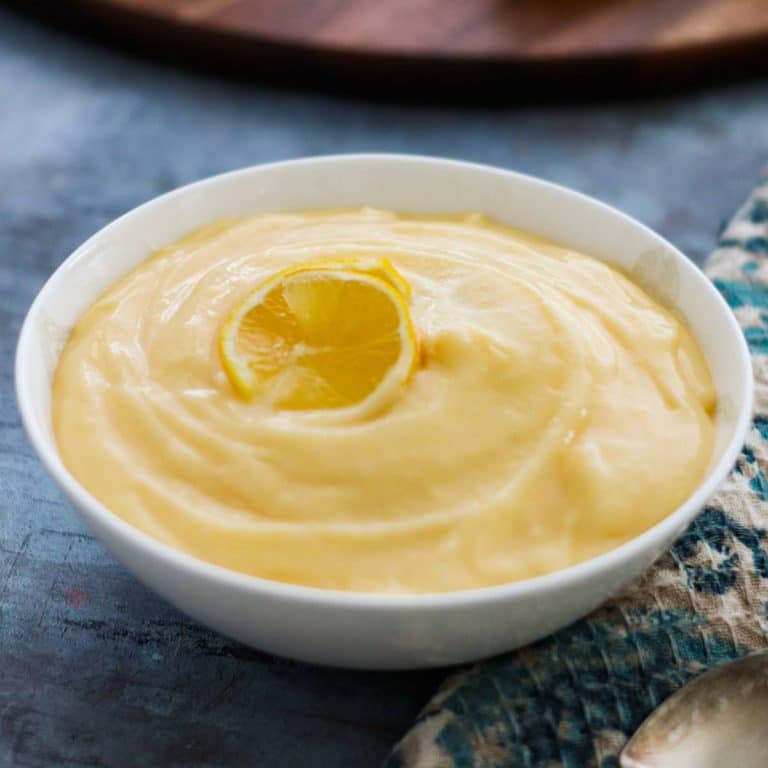 A bowl of lemon curd garnished with slices of lemon.