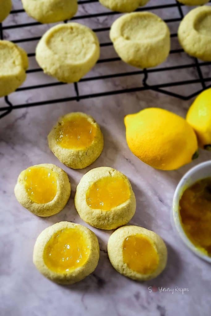 Lemon thumbprint curd cookies with some cookies on a rack and lemon nearby.