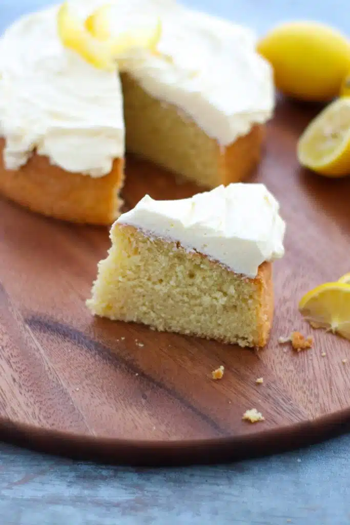 Lemon cake on a wooden chopping board with lemons next to it.