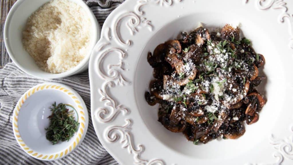 A dish of mushrooms with a bowl of permesand and a bowl of chopped parsley next to it.
