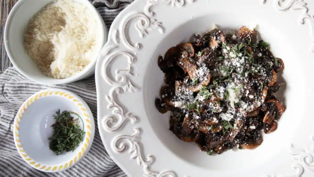 A dish of mushrooms with a bowl of permesand and a bowl of chopped parsley next to it.