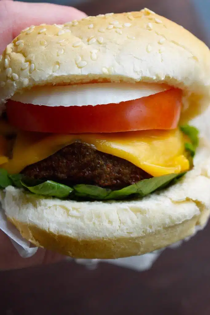 A hand holding burger buns filled with turkey burger, lettuce, tomato, onion, and cheese.