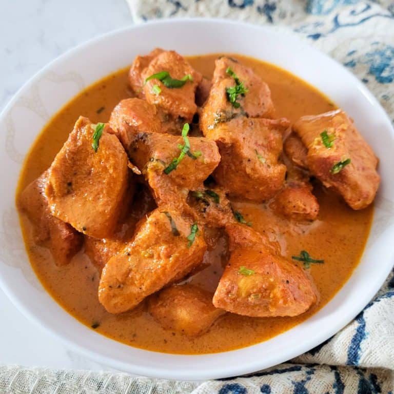 Butter chicken in a round white dish.