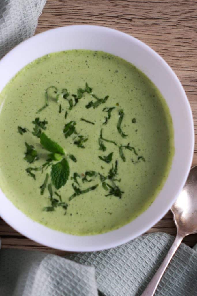 A bowl of cilantro mint chutney with a spoon next to it.