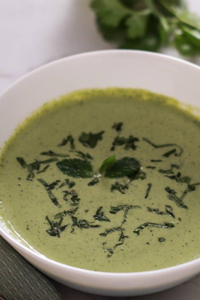 a bowl of green chutney garnished with chopped cilantro.