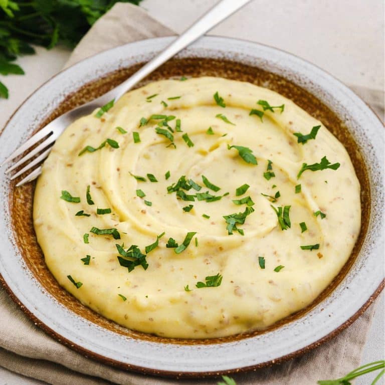 red skin mashed potatoes on a round dish garnished with chopped parsley.