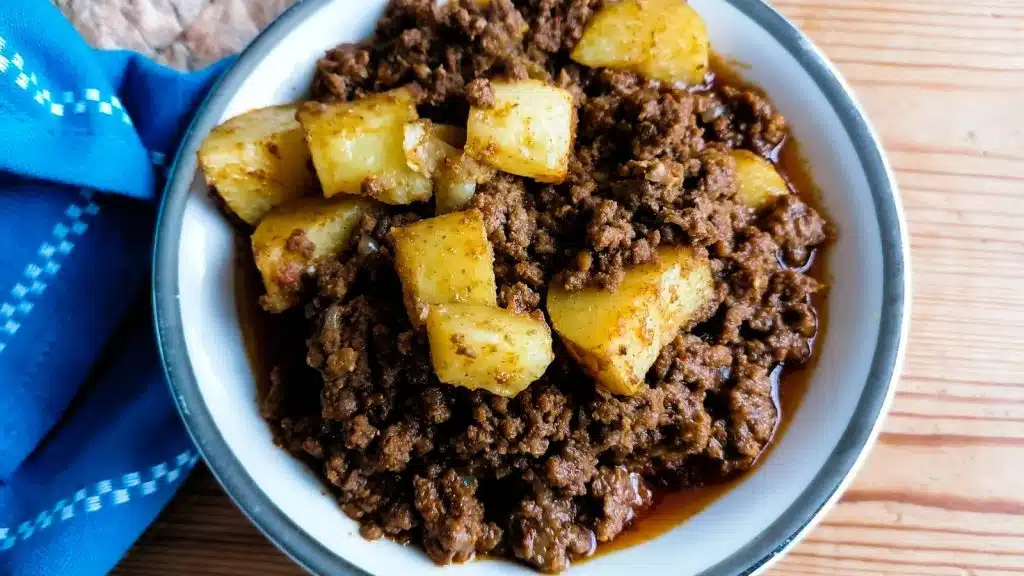 A bowl of meat and potato curry with blue napkin on the right side.