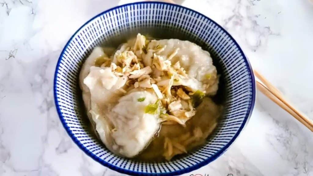 A bowl of chicken wontons with chopsticks on next to it.