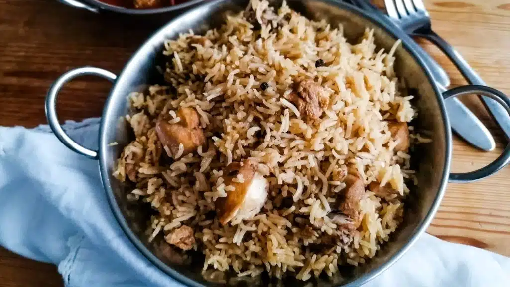 Chicken pilau rice in a metal dish with cutlery and white napkin in the background.