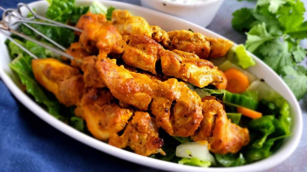 Chicken Tikka skewers with some salad on an oval dish.