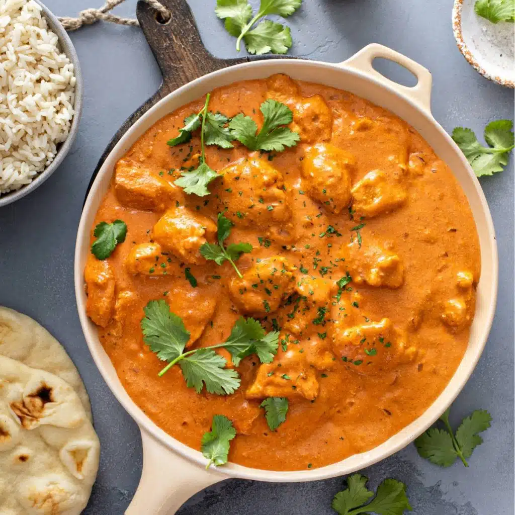 Chicken tikka masala in a frying pan with naan and rice next to it.
