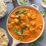Chicken tikka masala in a frying pan with naan and rice next to it.