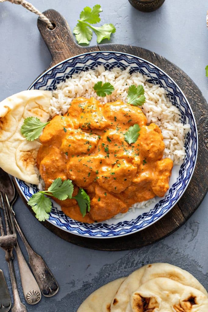 A plate of rice with chicken tikka masala and naan bread and garnished with chopped cilantro.