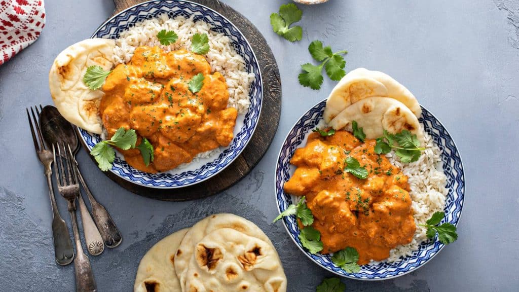 Plates of chicken tikka masala with rice and naan bread.