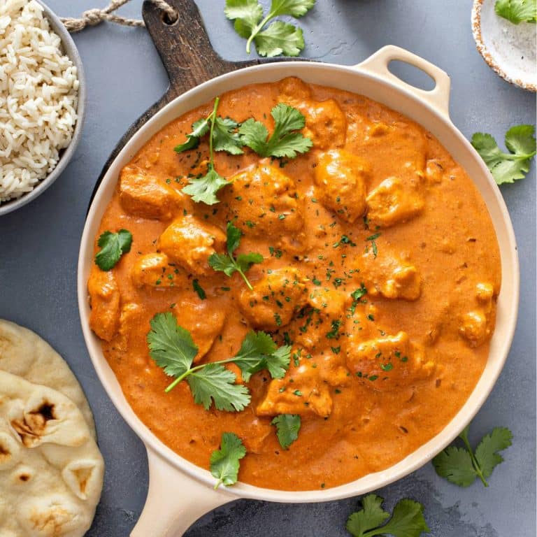 Chicken tikka masala in a frying pan with naan and rice next to it.