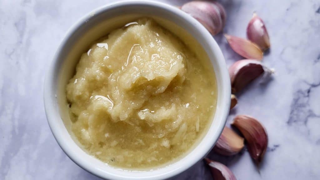 Garlic paste in a bowl and garlic cloves.