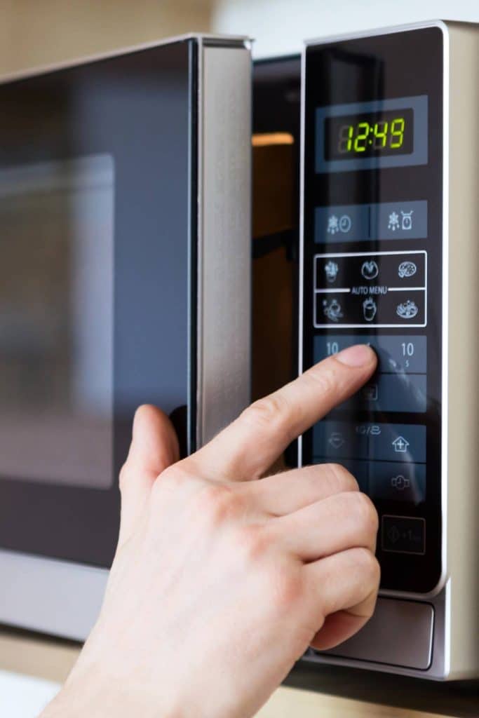 A hand touching buttons of a microwave.