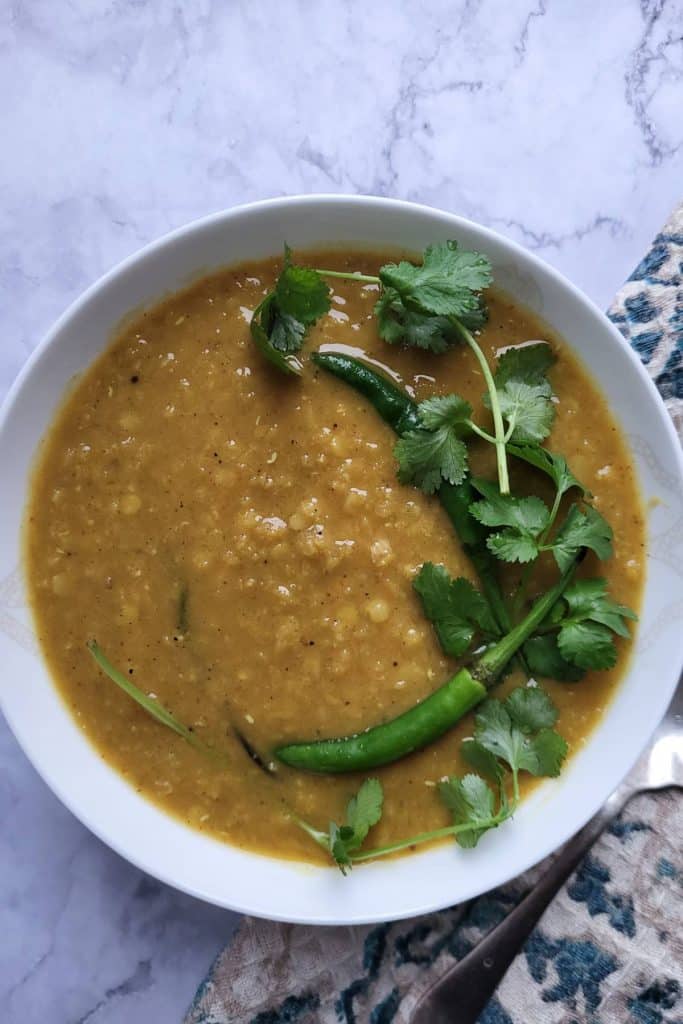 Masoor dal the red lentil curry in a white bowl, garnished with cilantro and green chilies.