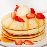 A stack of air fryer pancakes drizzled with maple syrup and topped with ice cream and strawberries.